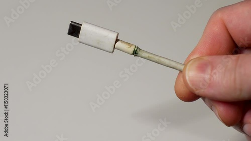 Broken charging cable, close-up. Hand holding frayed charging cable type C