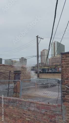 Chicago,USA.Dec,12,2024, Elevated view of an urban rooftop featuring a chimney emitting steam, with buildings and power lines creating a bustling cityscape in the background.