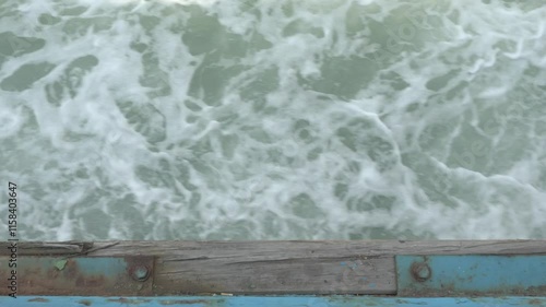 Watching waves from a top-down symmetry shot on a platform of an old ferry, bubbles splashing and waves lightly crashing, with a cigarette butt stuck in the wooden frame.
