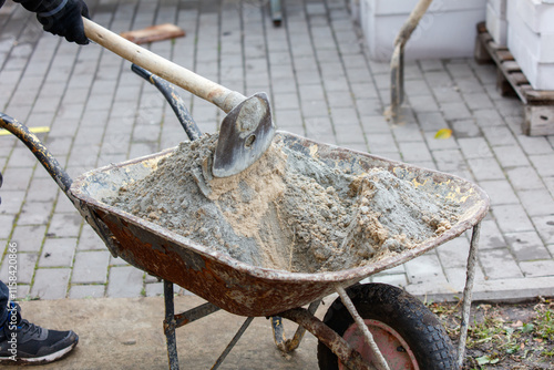 A person is shoveling sand into a wheelbarrow photo