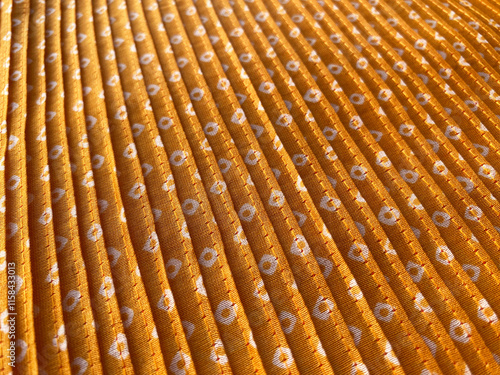 A close-up view of intricate white bandhani block prints adorning mustard silk fabric, enhanced by delicate pleating. photo