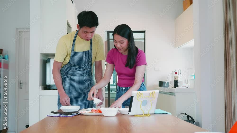A man and woman are cooking together in a kitchen. The man is wearing an apron and the woman is wearing a pink shirt. They are using a tablet to follow a recipe A man and woman are cooking together in a kitchen. The man is wearing an apron and the woman is wearing a pink shirt. They are using a tablet to follow a recipe