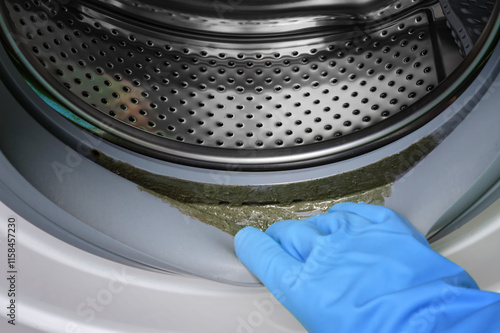 Close-up a person hand in blue gloves checks the dirt on the rubber of a washing machine.The dirty rubber gasket with mold  on washing machine. photo