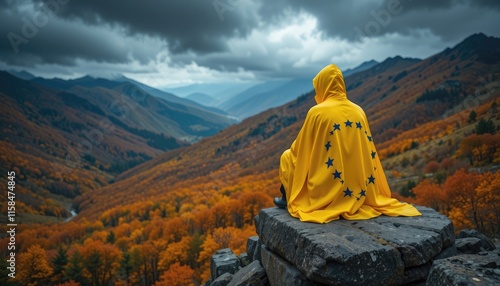 Person in yellow hooded cloak overlooking autumn mountain valley photo