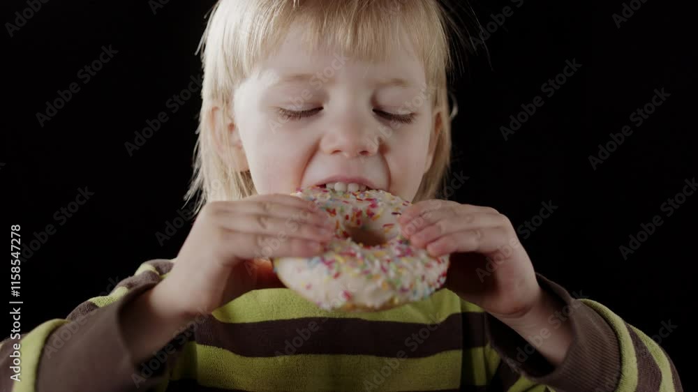 Adorable smiling girl takes big bite of glazed donut with sprinkles, frontal Adorable smiling girl takes big bite of glazed donut with sprinkles, frontal