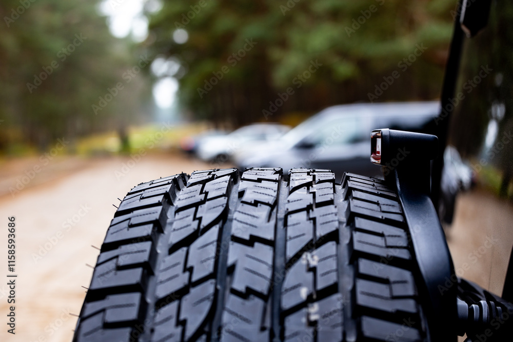 Deep tread of a new off road tire mounted on the rear door of an off-road vehicle. The photo was taken during the day.
