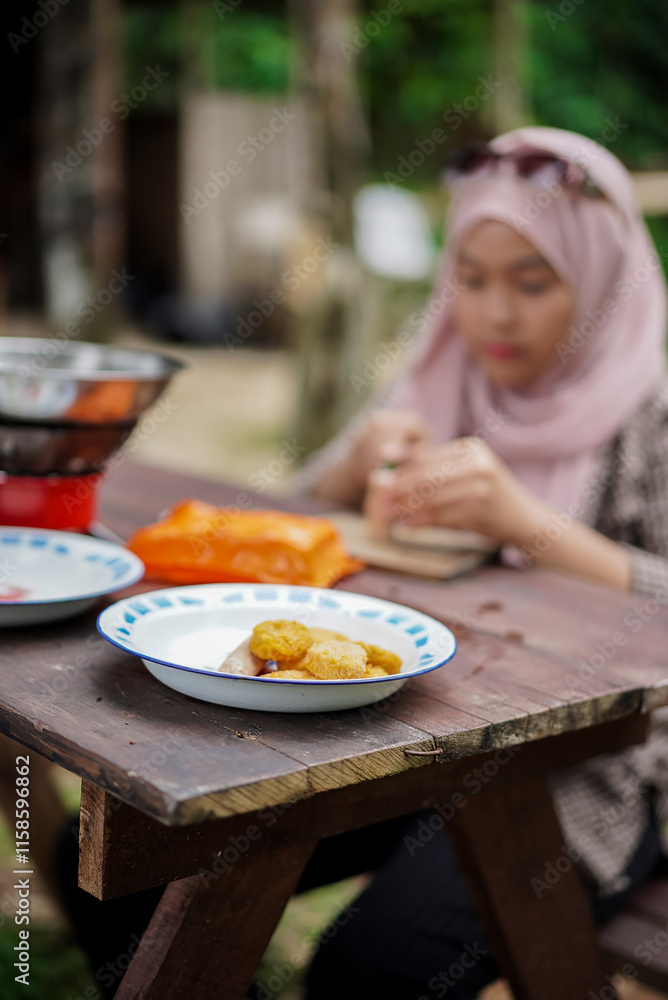 young Indonesian woman in hijab slicing sausages while camping in a forest cabin, travel concept. young Indonesian woman in hijab slicing sausages while camping in a forest cabin, travel concept.