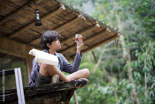 Young Indonesian man reading a book while enjoying a cup of coffee while relaxing in a jungle cabin, travel concept. photo