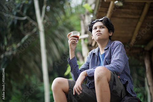 young Indonesian man relaxing in a forest cabin while enjoying a cup of coffee, travel concept. photo