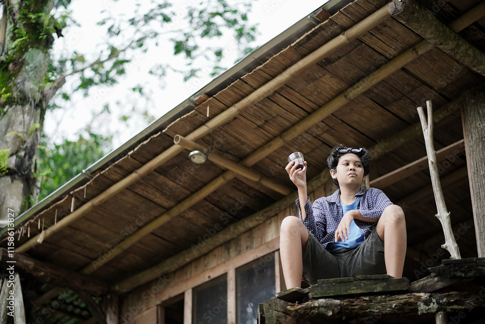 young Indonesian man relaxing in a forest cabin while enjoying a cup of coffee, travel concept. young Indonesian man relaxing in a forest cabin while enjoying a cup of coffee, travel concept.