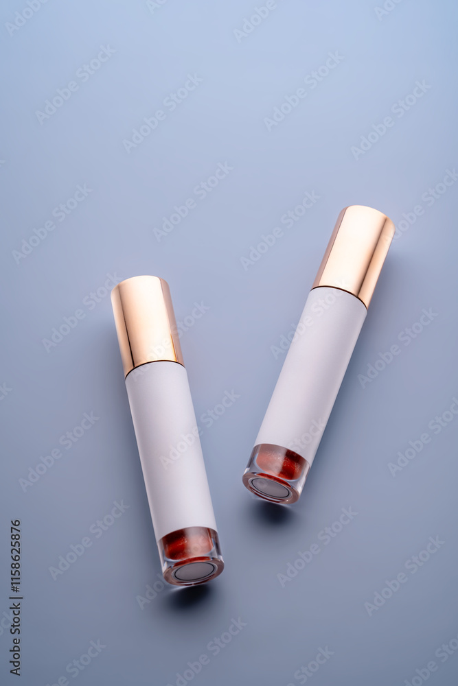 Top view of two closed lip gloss tubes with red shimmering gloss and blank label for design. Luxury cosmetic product packaging with golden caps on gray-blue background. Showcase presentation, Top view of two closed lip gloss tubes with red shimmering gloss and blank label for design. Luxury cosmetic product packaging with golden caps on gray-blue background. Showcase presentation,