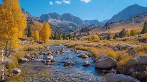 Scenic autumn mountain river flowing through golden aspen trees and rocky landscape under a clear blue sky.
