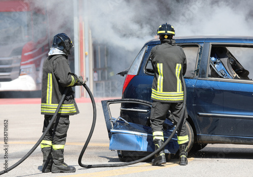 team of firefighters extinguishing the car with the hose of the firefighting nozzle photo