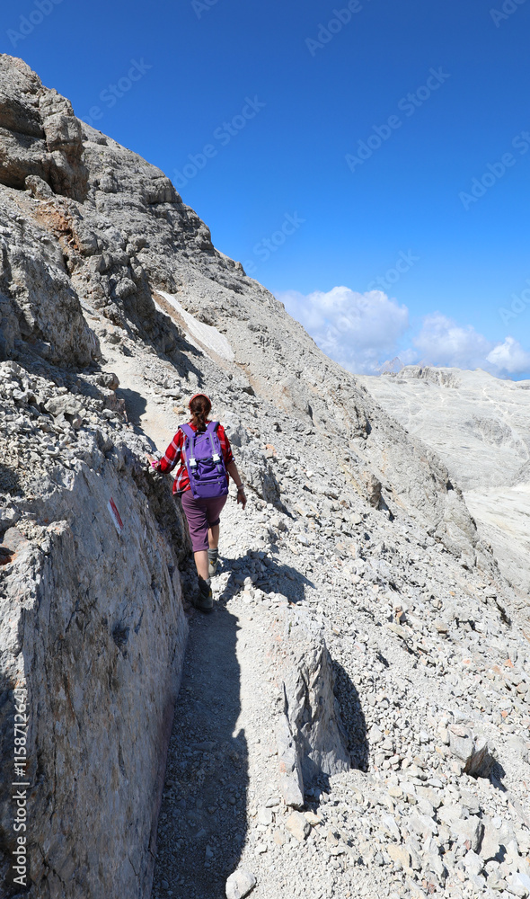woman with a backpack walking along a narrow rugged trail in the rocky mountains during the summer woman with a backpack walking along a narrow rugged trail in the rocky mountains during the summer