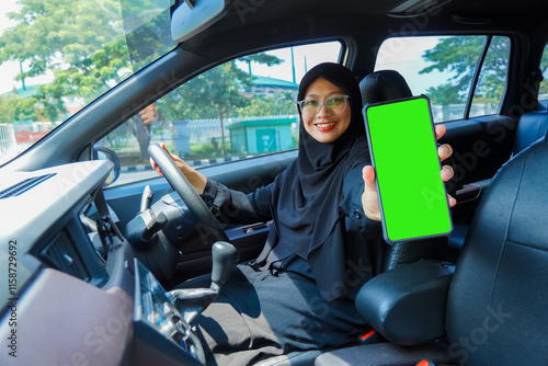A woman in a black hijab is holding a green phone in a car. She is smiling and she is happy