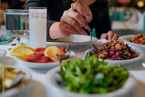 Close up shot of the woman take mezes and sining table Filled with Turkish Raki and Seafood in a Cozy Restaurant. The image showcases vibrant mezes, raki glasses, and a warm dining ambiance. photo