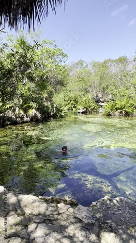 Heart Cenote in Mexico with crystal-clear waters and visible stones. A person happily jumping into the water. Warm, blue-green waters perfect for a family vacation in Yucatán, Mexico.