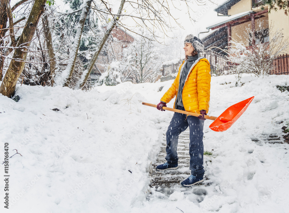 Portrait of a woman with a snow shovel removing snow from her yard at a country house.