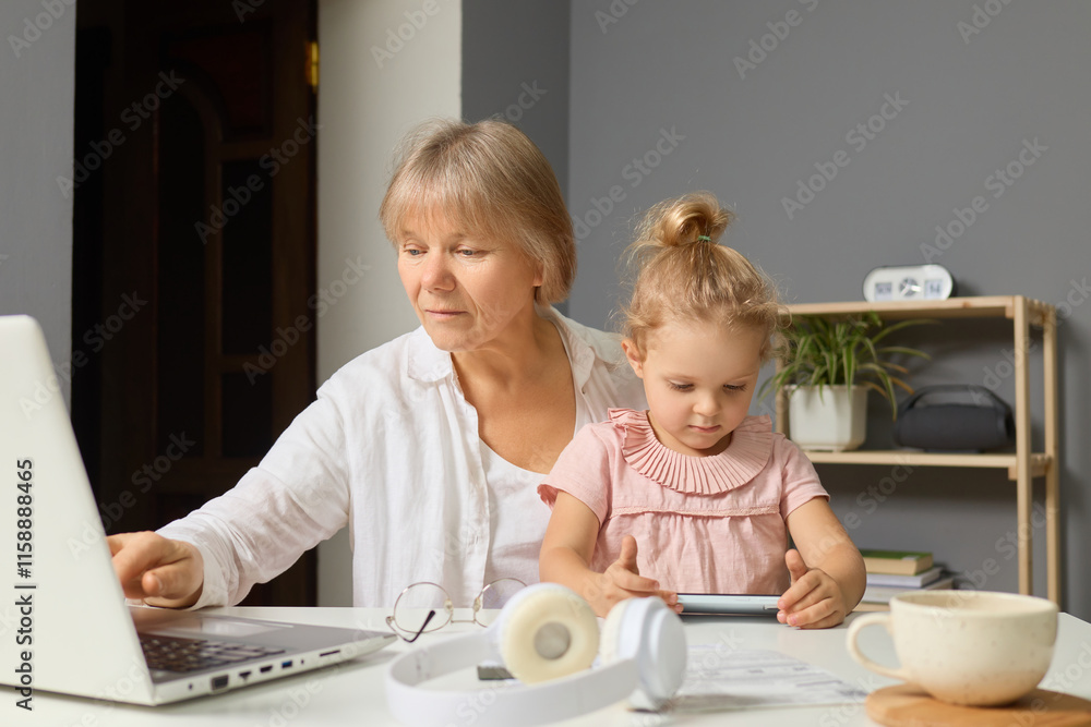 A grandmother helps her young granddaughter with an online learning activity while sitting at a table in a cozy home environment during the afternoon A grandmother helps her young granddaughter with an online learning activity while sitting at a table in a cozy home environment during the afternoon