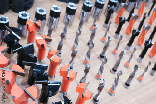 Table full of different sized drill bits. The drill bits are of various sizes and colors, including black, orange, and silver. The table is cluttered with the drill bits photo