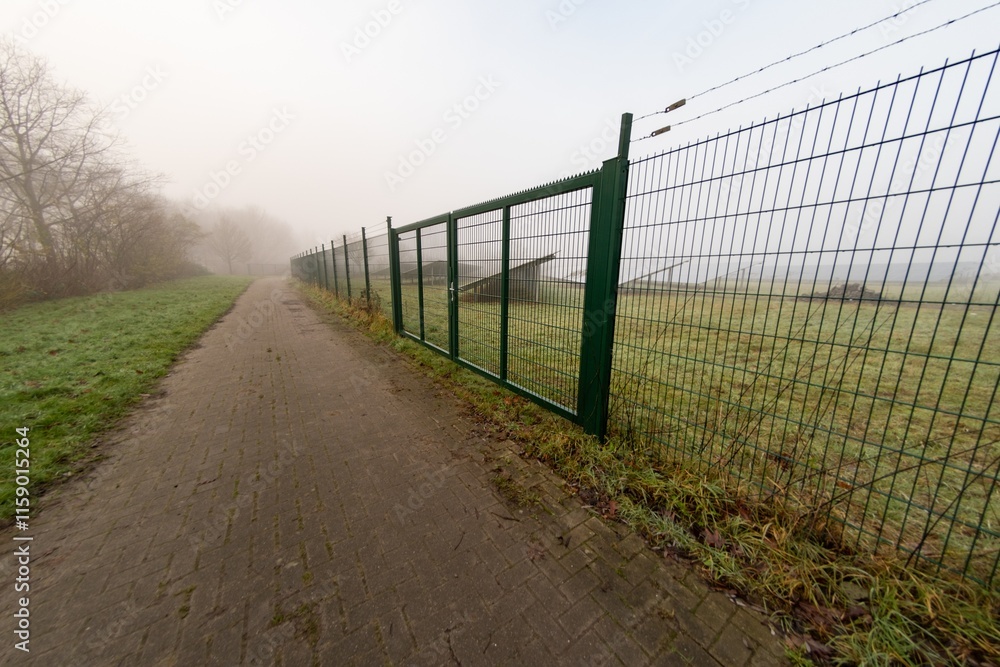 Barbed wire fence protecting solar panels along a misty brick path Barbed wire fence protecting solar panels along a misty brick path