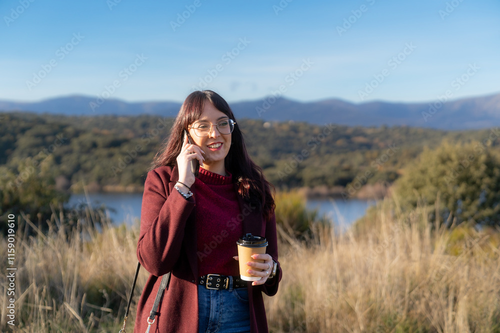 Young woman talking on phone and drinking coffee by the lake