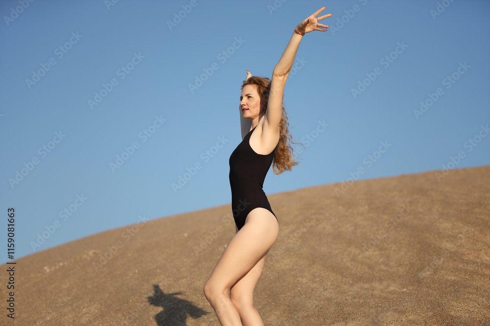A woman in black swimsuit poses gracefully on a sandy hill under the blue sky A woman in black swimsuit poses gracefully on a sandy hill under the blue sky
