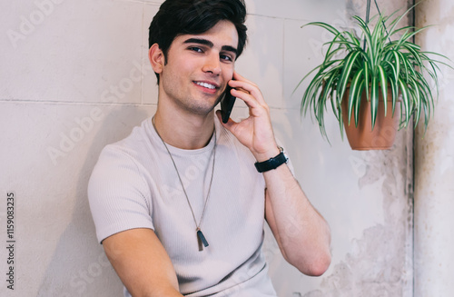 Portrait of handsome caucasian male in stylish casual wear enjoying positive conversation on free time, 20s hipster guy millennial looking at camera using cheap tariffs for mobile phone calls photo