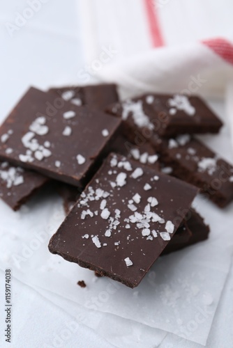 Pieces of chocolate with salt on white table, closeup