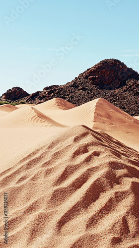 Sandy dunes with textured patterns under clear blue sky and rocky hills photo