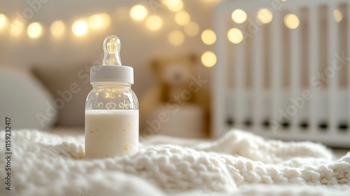 1. A baby bottle filled with milk placed on a soft white blanket with a blurred nursery in the background photo