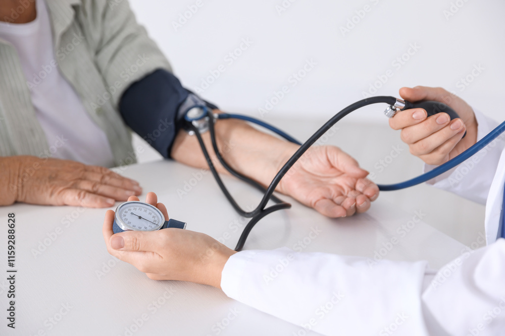 Doctor measuring patient's blood pressure at table in hospital, closeup Doctor measuring patient's blood pressure at table in hospital, closeup