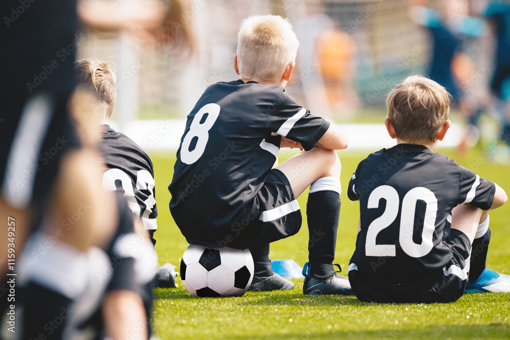 Fototapeta premium Kids in the Sports Team Sitting on Pitch Sideline. Young Football Players. Young Soccer Team Sitting on Bench. Soccer Match For Children. Young Boys Playing Tournament Soccer Match. Youth Soccer Club