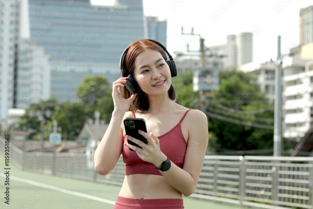 Short haired sporty girl with headphones in sportswear use smartphone after jogging outdoor. Happy smiling Asian woman hold mobile phone to listen music while walking exercise on city street outside. Short haired sporty girl with headphones in sportswear use smartphone after jogging outdoor. Happy smiling Asian woman hold mobile phone to listen music while walking exercise on city street outside.