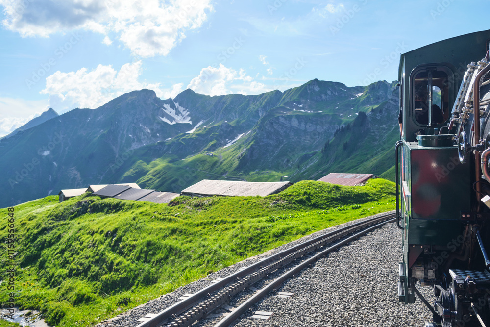Fototapeta premium Scenic view from a vintage train traveling through the lush green hills of Switzerland, with the stunning Alps in the background. Experience the beauty of Brienz.