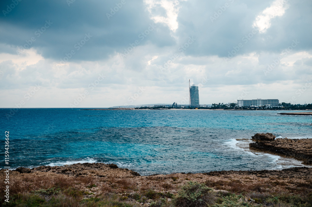 Fototapeta premium Coastal View with Rocky Shoreline and Distant Buildings