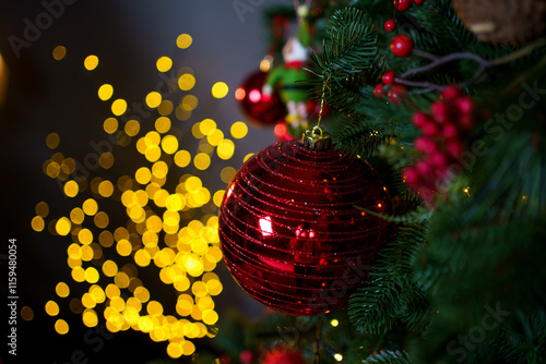 Festive red ornament hangs on Christmas tree surrounded by warm glowing lights
