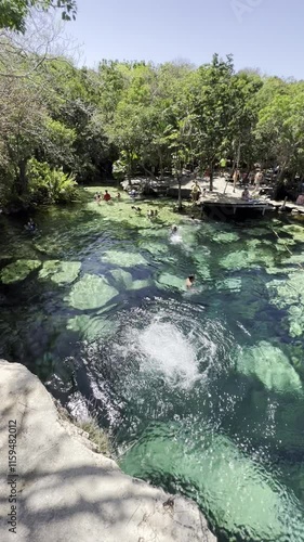 Heart Cenote in Mexico with crystal-clear waters and visible stones. A person happily jumping into the water. Warm, blue-green waters perfect for a family vacation in Yucatán, Mexico.