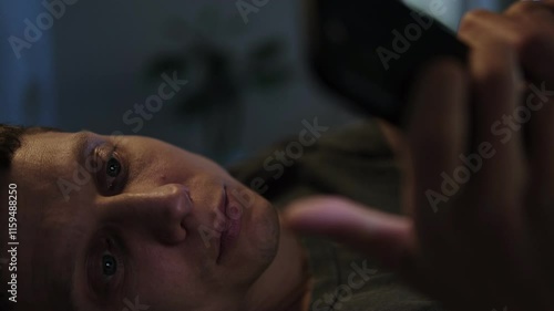 Close-up of a man scrolling through his phone in bed at night, struggling with sleep disruption caused by social media and short-form video content. photo