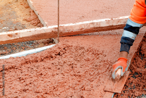 Builder applying smooth finish to freshly poured concrete in outdoor construction site during daylight hours photo