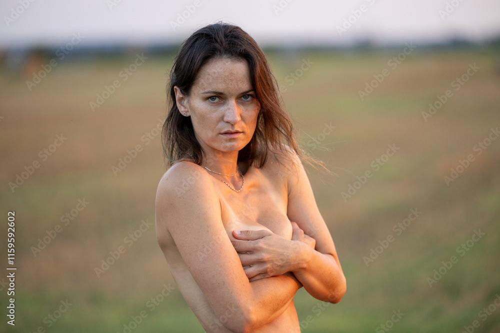 Contemplative woman at dusk, shielding herself with crossed arms against a serene field backdrop Contemplative woman at dusk, shielding herself with crossed arms against a serene field backdrop