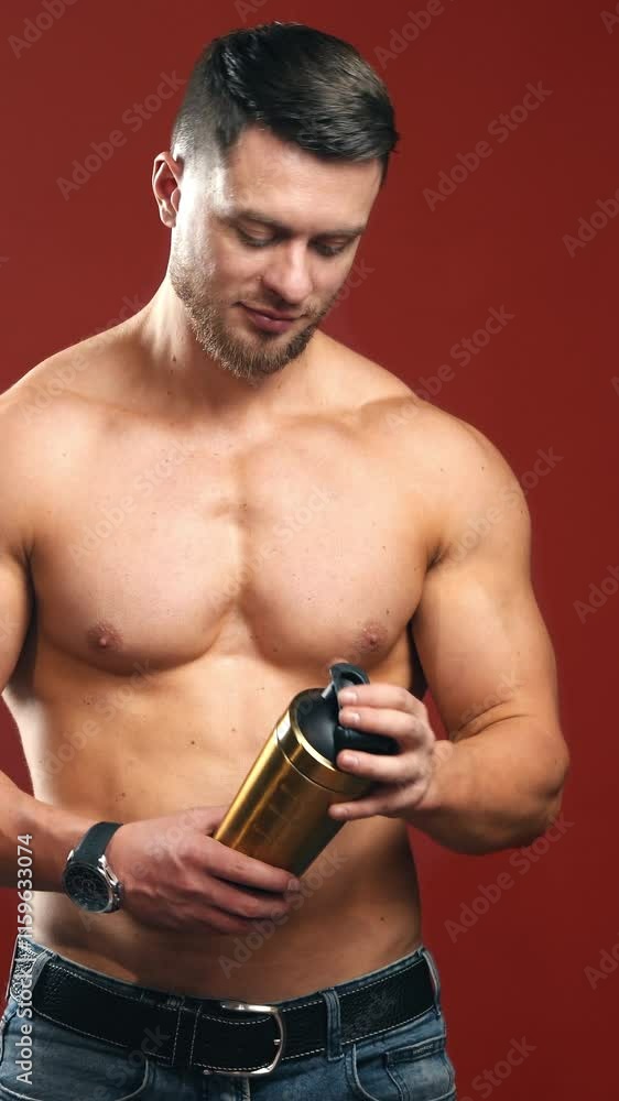 Sporty man with flask in studio. Muscular male model without shirt on the dark red background indoors. Athlete drinking water. Vertical video Sporty man with flask in studio. Muscular male model without shirt on the dark red background indoors. Athlete drinking water. Vertical video