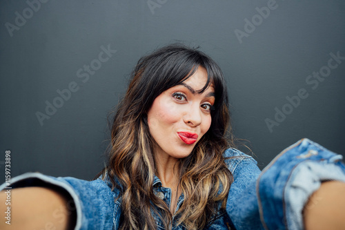 Obraz na plátně Portrait of a cheerful stylish woman taking a selfie while pouting against a gra