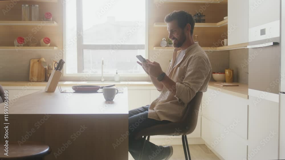 Man Relaxing with Smartphone at Kitchen Counter Man Relaxing with Smartphone at Kitchen Counter