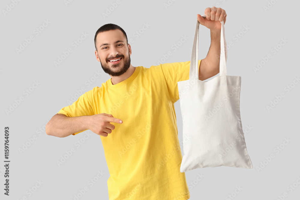 Young man pointing at textile bag on light background Young man pointing at textile bag on light background