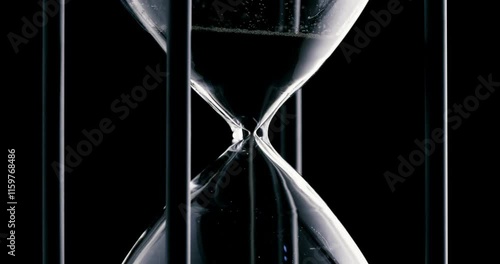 Rotation of sand timer clock with sand flowing from through hourglass on black background.

