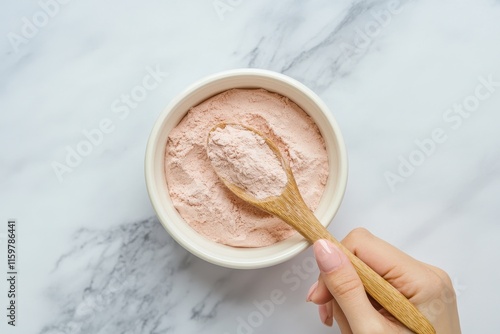 Bowl of collagen powder and wooden spoon on marble surface Mixing collagen into strawberry yogurt Woman s hand photo