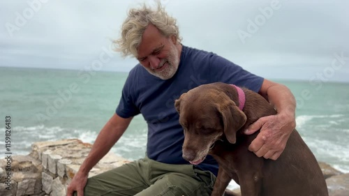 portrait of senior latino man bonding with his dog outdoors with ocean in background