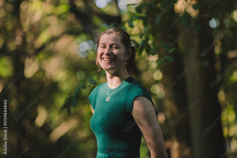 A woman in a green dress stands amidst tall trees in soft sunlight, her smile radiating warmth and her surroundings rich with forest tones and depth A woman in a green dress stands amidst tall trees in soft sunlight, her smile radiating warmth and her surroundings rich with forest tones and depth