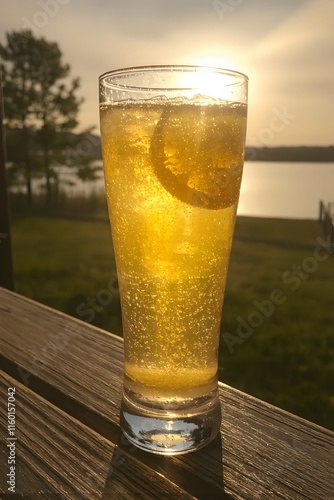 Golden Hour Fizz: Sparkling refreshment on a lakeside deck at sunset. A tall glass of bubbly beverage with a lemon slice, bathed in the warm glow of the evening sun.